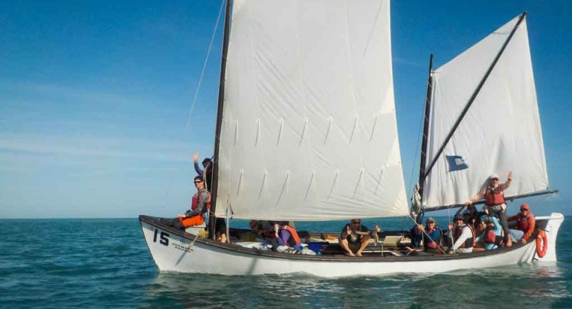 a sailboat full of people sits on calm water on an outward bound course